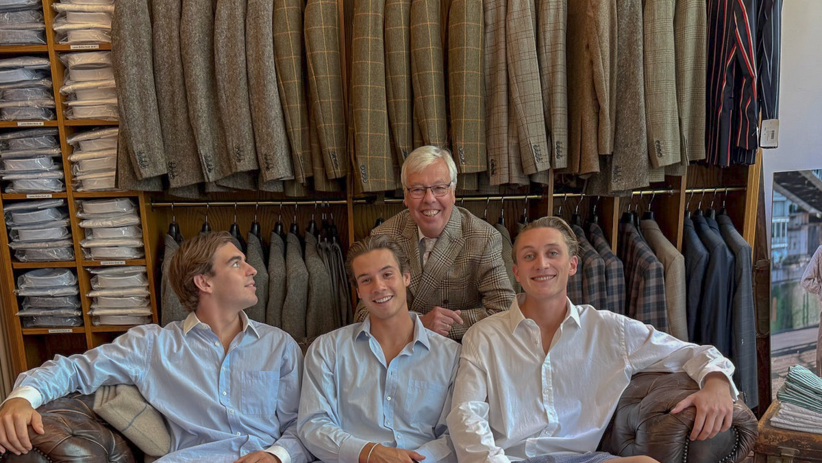 Four men on a leather sofa in front of shelves with jackets and folded shirts in a shop – John Crocket