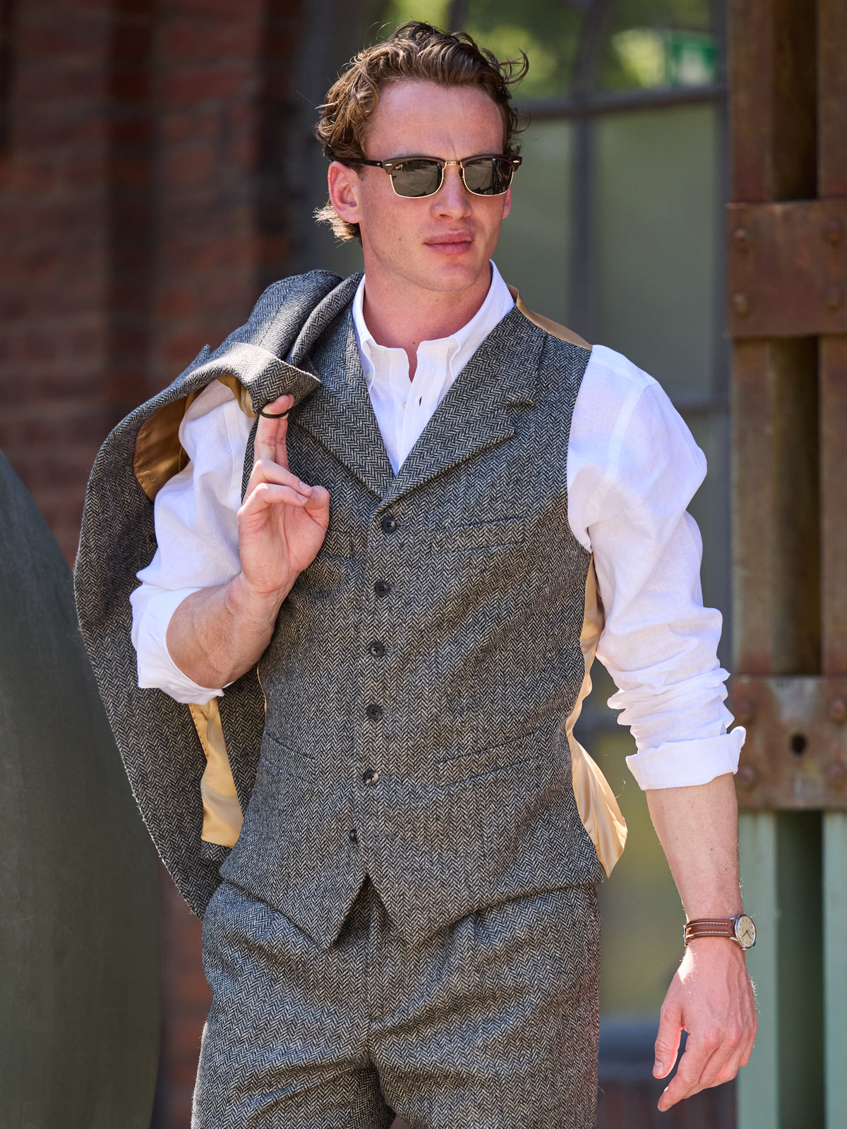 Dark Grey tweed suit in Moon Tweed, waistcoat with an open-necked shirt, jacket over the shoulder – John Crocket