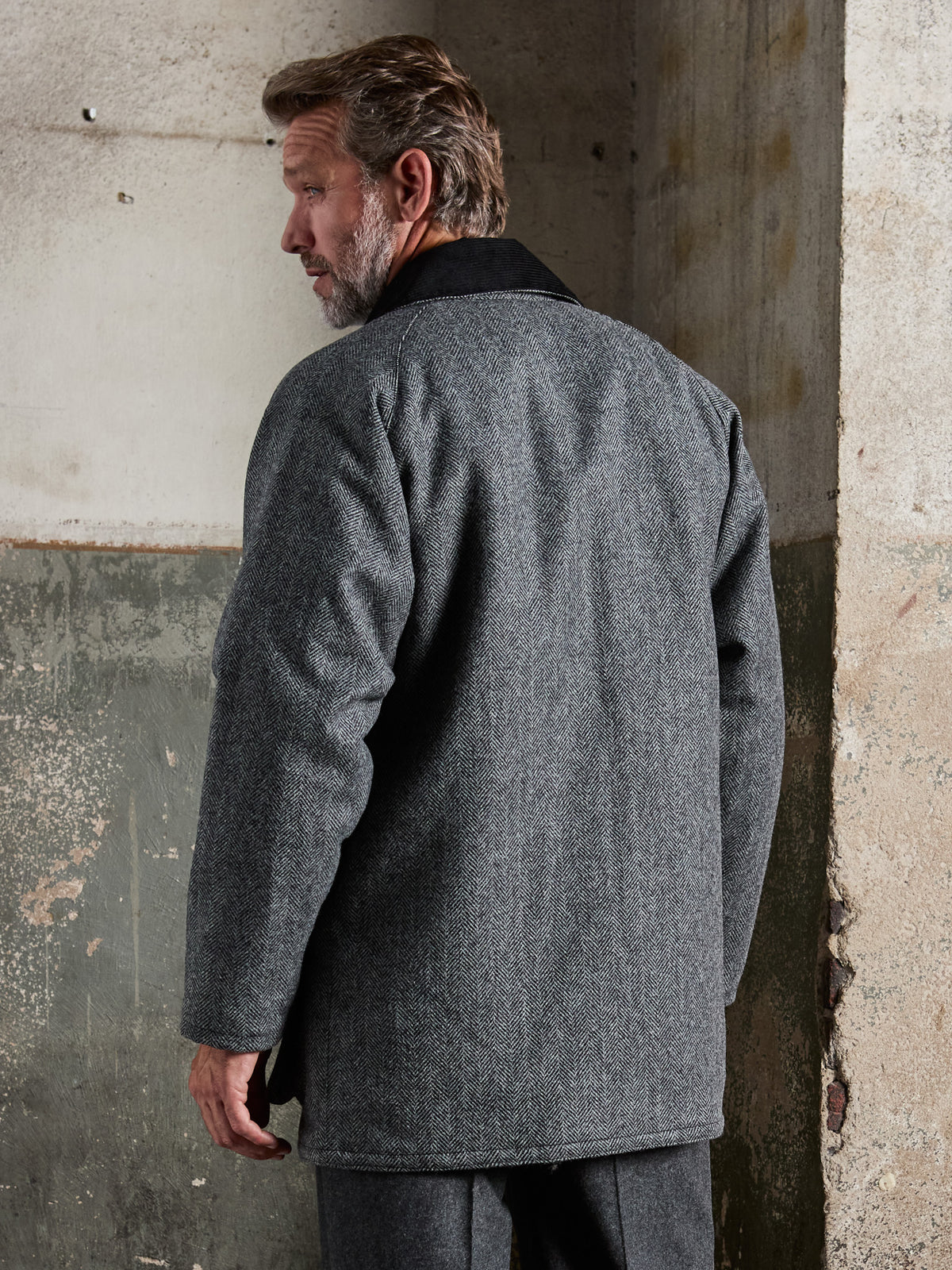 Oxford Jacke Fischgrät Moon Tweed Dark Grey Rückansicht am Model vor Betonwand — John Crocket