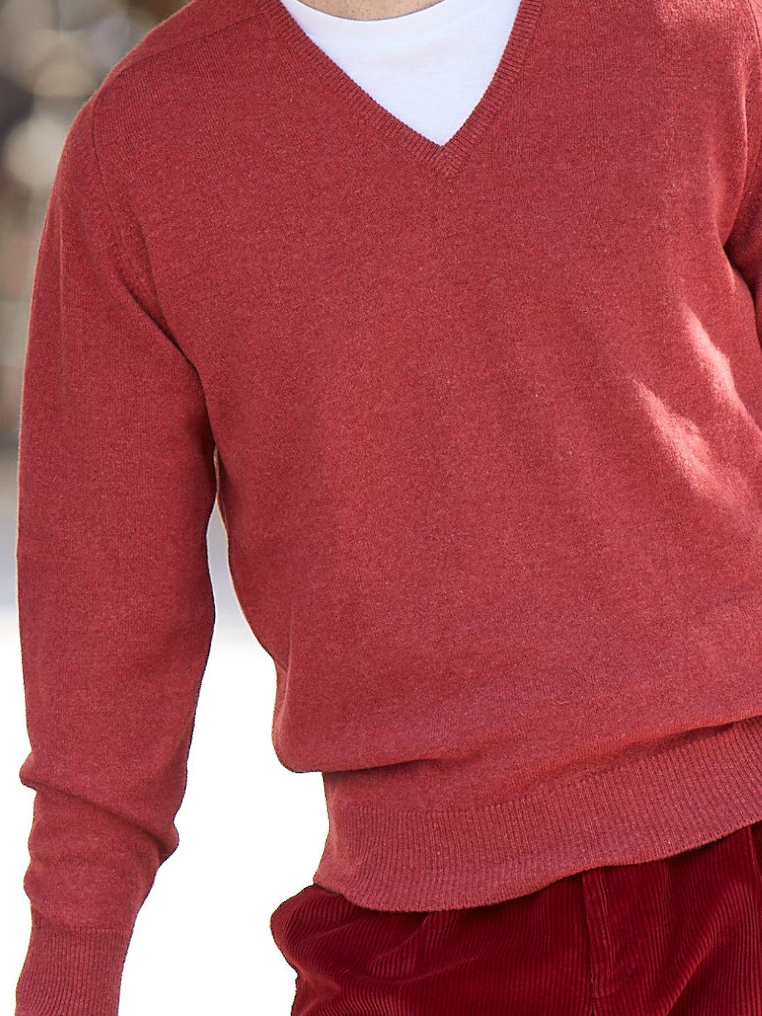 Lambswool V-neck jumper in marled red, worn by the model with a white T-shirt and red corduroy trousers – John Crocket