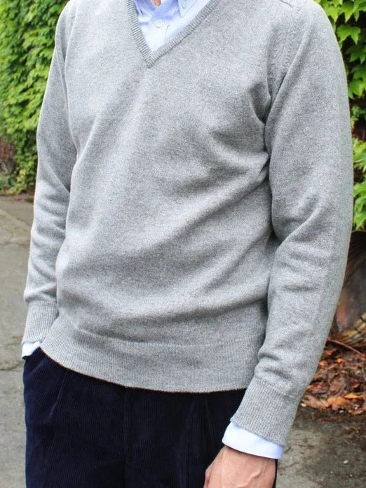 Lambswool V-neck jumper in light grey, worn by the model with a light blue shirt and corduroy trousers – John Crocket