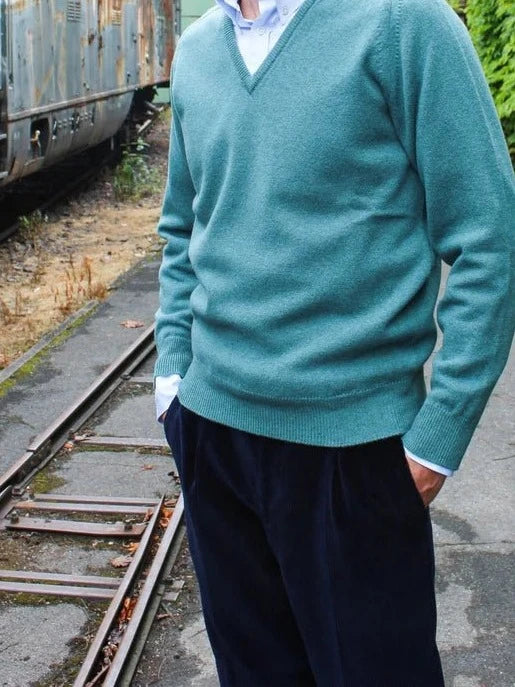 Lambswool V-neck jumper in turquoise green, worn by the model with a light blue shirt and dark corduroy trousers – John Crocket