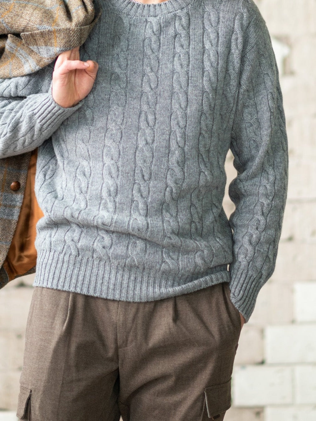 Cashmere cable-knit jumper (6-ply) in Flannel (grey), shown worn, with a jacket over the shoulder – John Crocket
