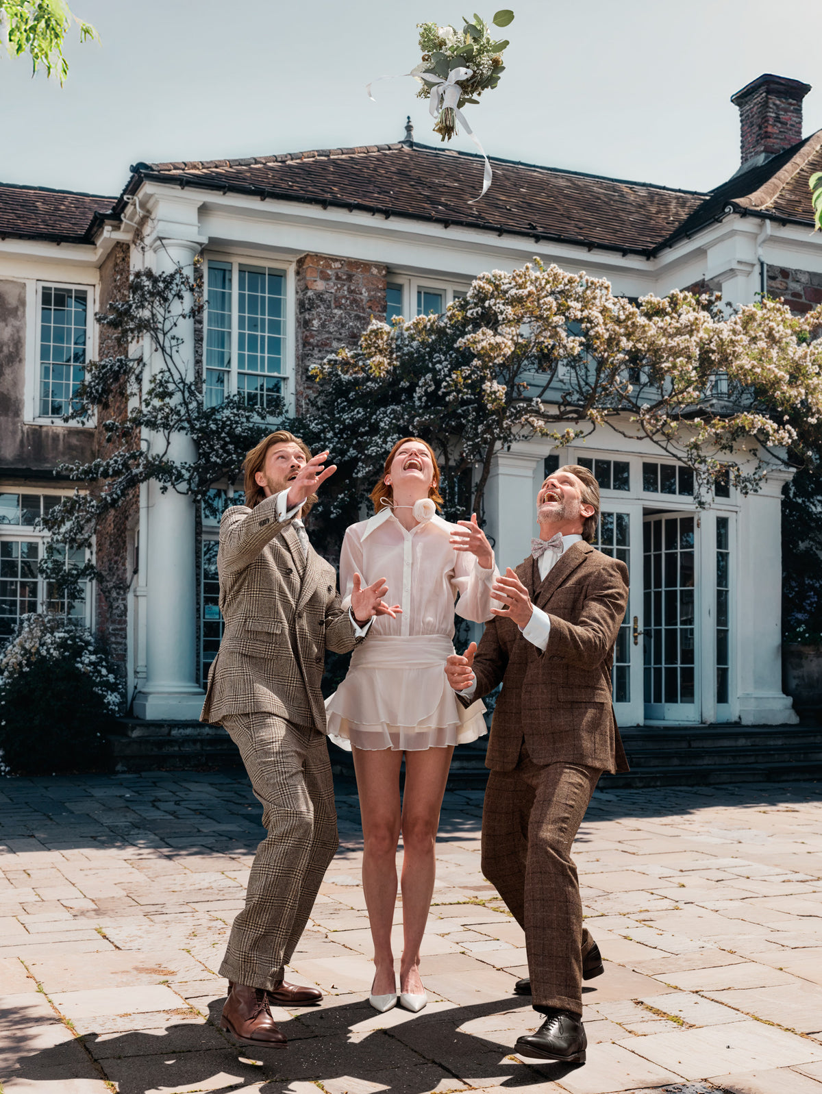 Bride between two men in checked tweed suits, the bridal bouquet flying through the air — John Crocket