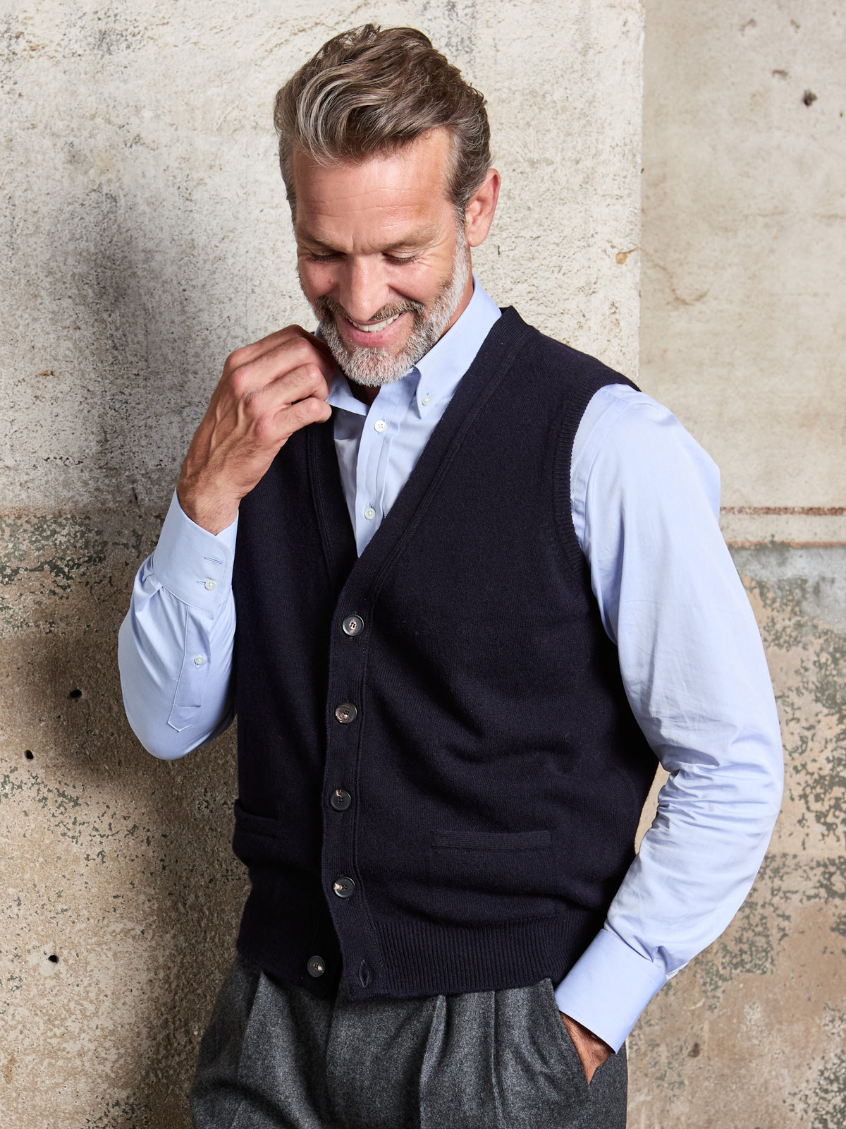Lambswool sleeveless cardigan with button placket in Navy, hand at the collar, worn, front view – John Crocket
