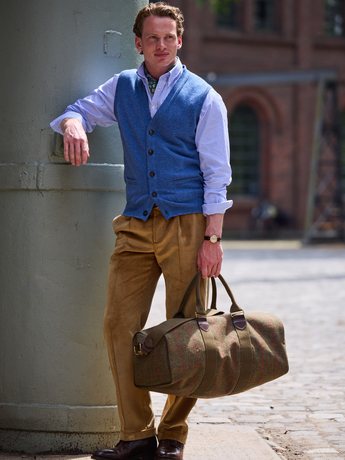 Weekender in Lovat Tweed, Olive, with red windowpane check, carried in the hand with a blue sleeveless cardigan and corduroy trousers – John Crocket