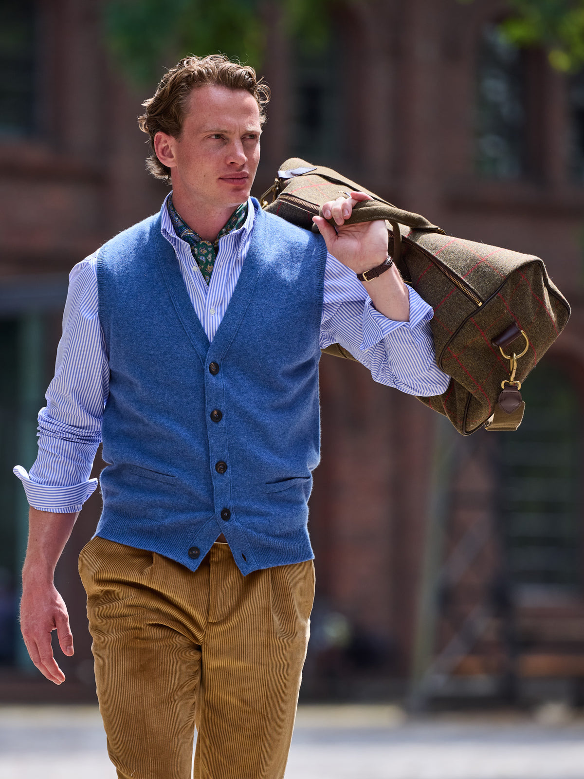 Weekender in Lovat Tweed, Olive, hung over the shoulder by the handles, with a blue sleeveless cardigan – John Crocket
