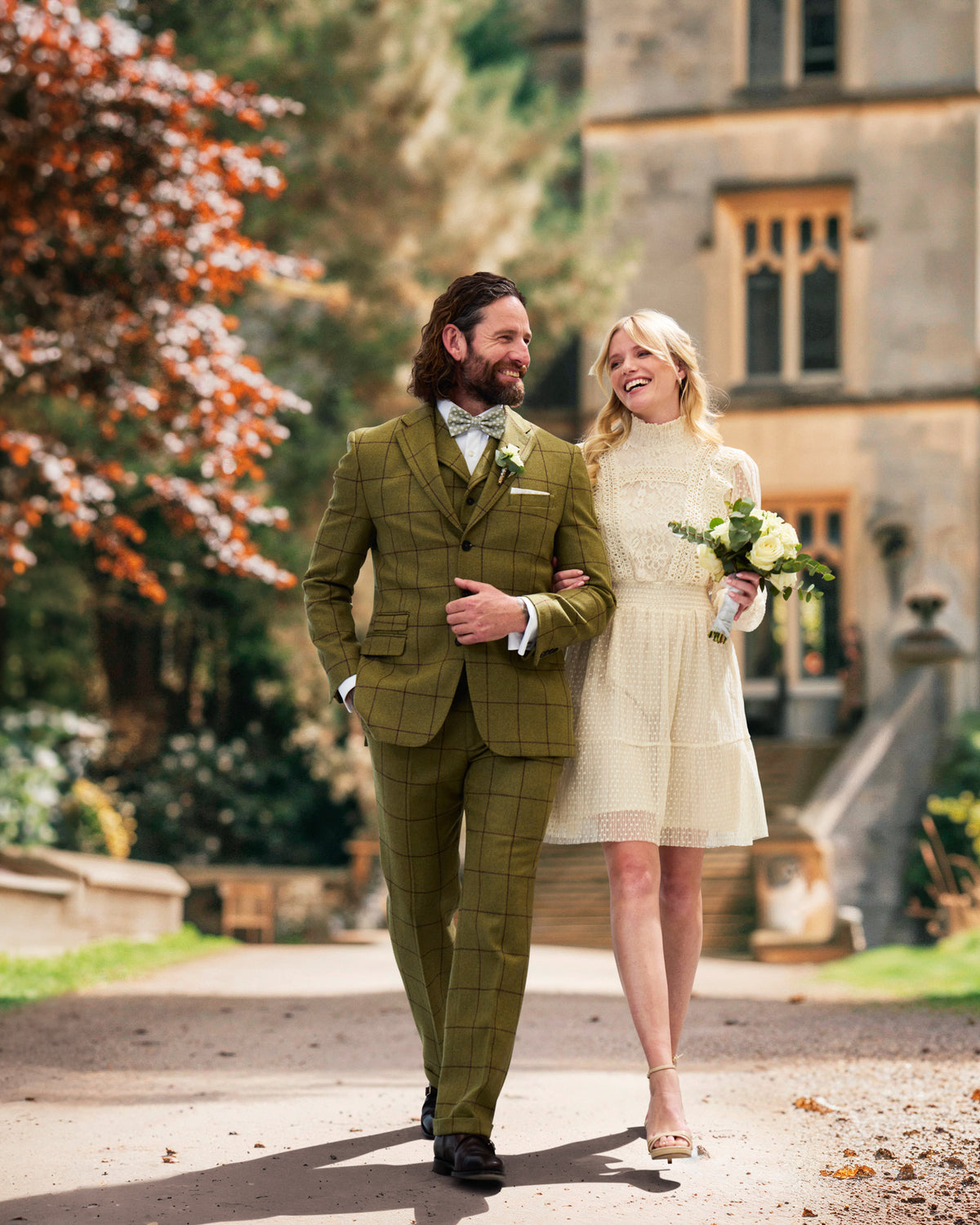 Bride and groom arm in arm, groom in a green checked tweed suit with bow tie, bride in a light dress — John Crocket