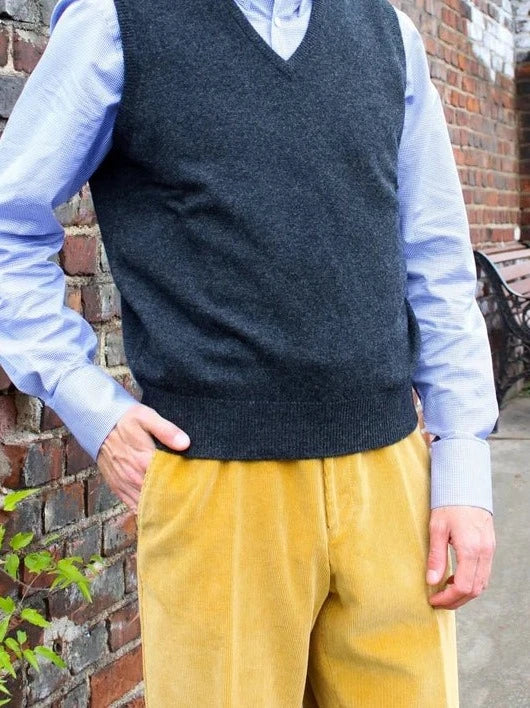 Lambswool spencer met V-hals in antraciet, gedragen door model met lichtblauw overhemd en gele ribbroek – John Crocket