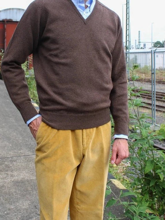 Lambswool V-neck jumper in brown, worn by the model with a light blue shirt and yellow corduroy trousers – John Crocket